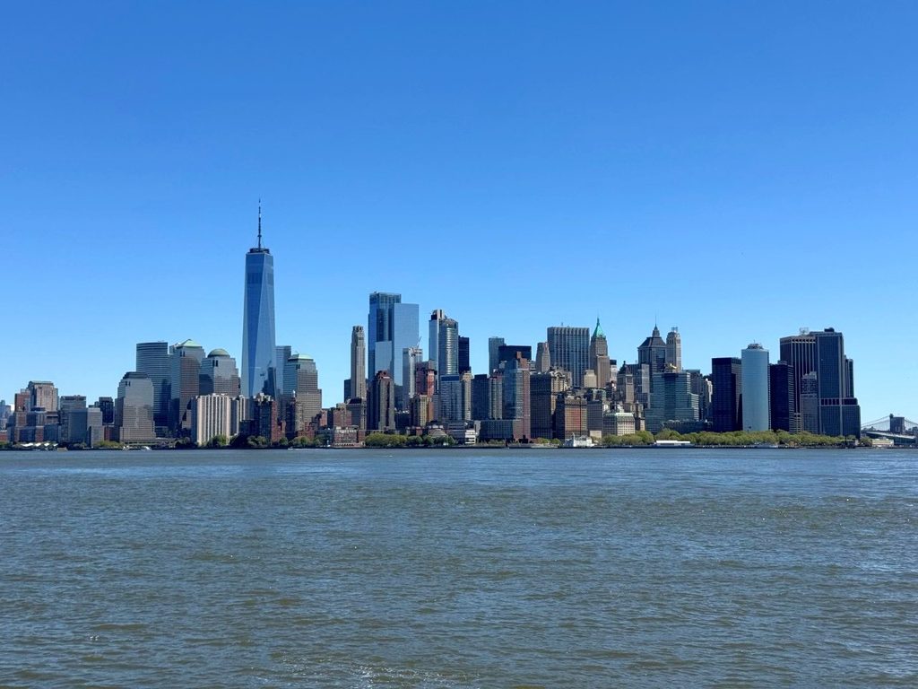 New York City skyline across the water with One World Trade Center visible on a clear day.